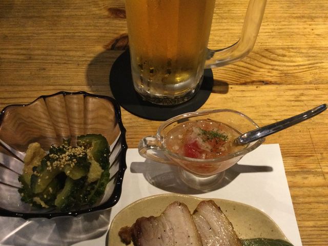 お通しは揚げとゴーヤの煮物(お客ごとに違った)名物シュラスコの豚バラ焼き、エビス生_源ZO-NE