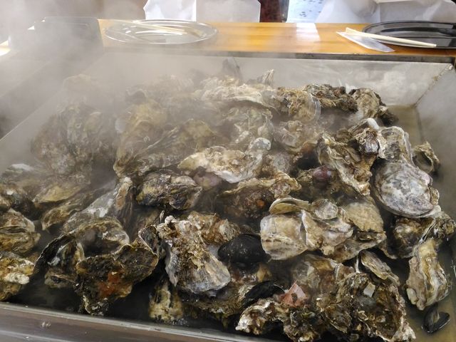 テーブルの真ん中に鉄板があり、蓋をして蒸し焼きにします。1テーブル約6人で焼き牡蠣を囲みます。_かき小屋