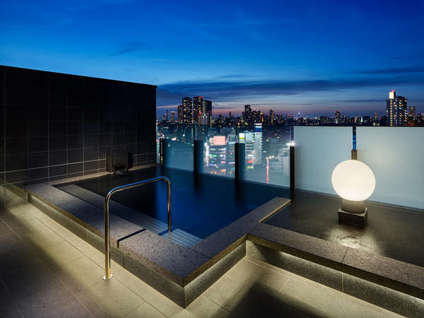 男性大浴場　外湯【夜】新宿・六本木方面の夜景が一望でき、見晴らしのよい開放的な空間です。