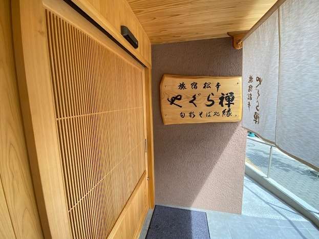 樅ノ木に書き下ろされた館名文字。大きな桧製の自動ドアがお客様をお迎えします。