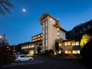 *夕暮れから夜へと移ろう時間帯の外観。灯りがともる館内が、安心感のある滞在を印象づけます。